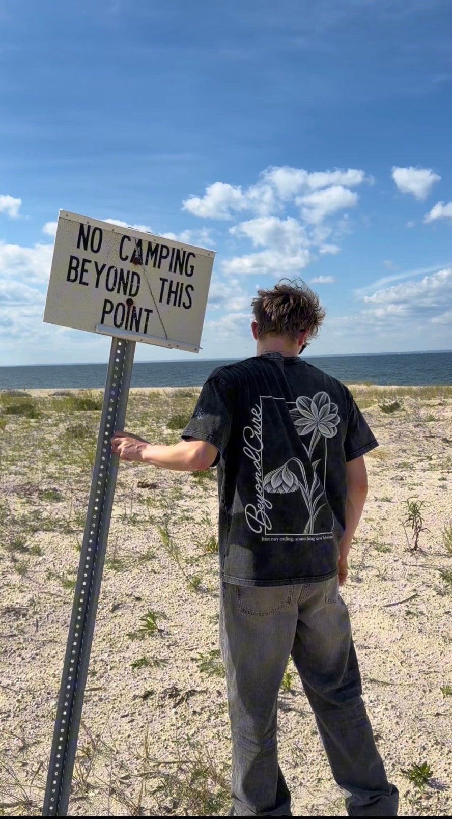 BeyondCure beach campaign beside the Beyond This Point sign, showing the back graphic
